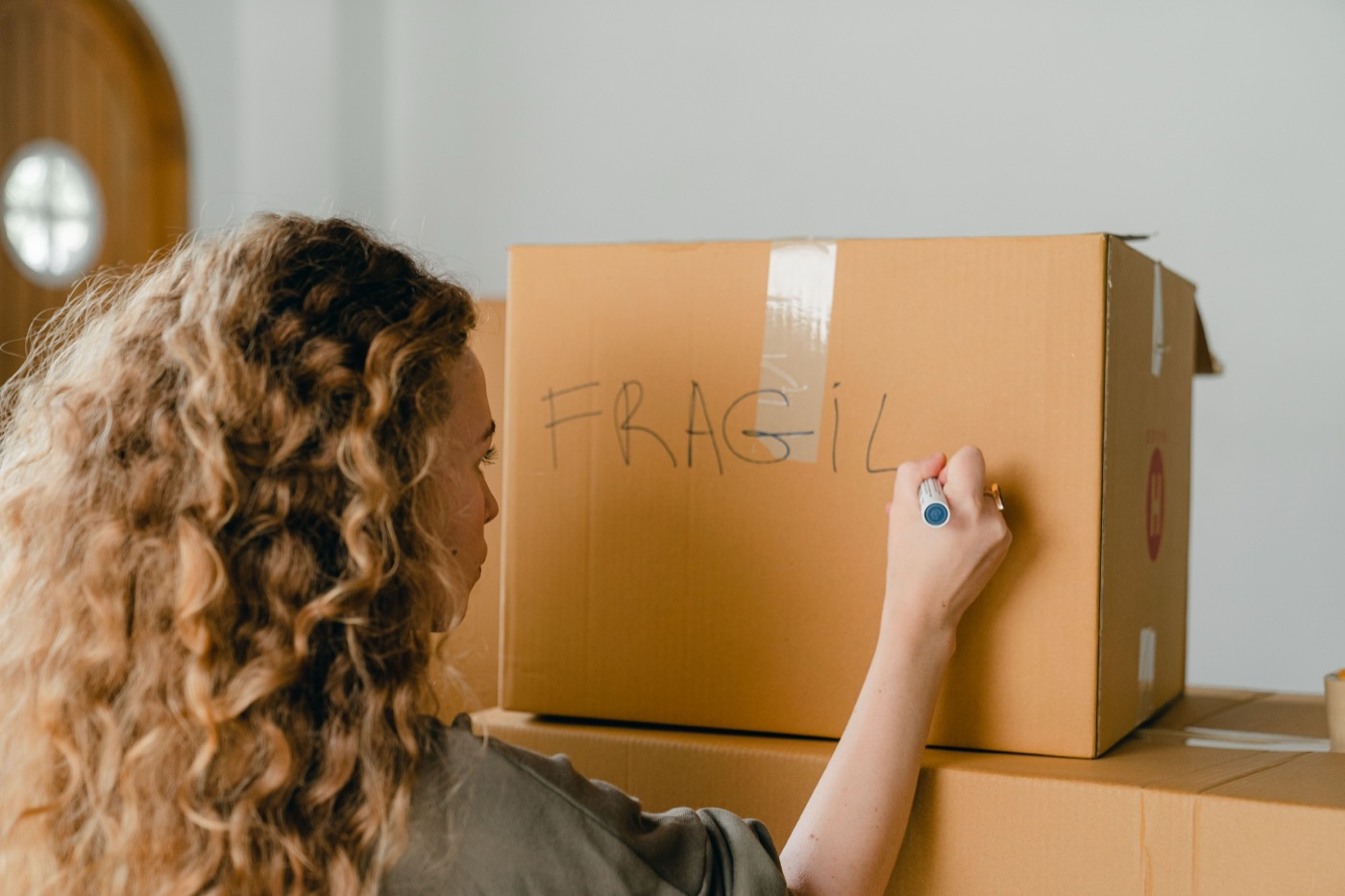 A woman labels a cardboard moving box with a marker, packing up to move out of a rental